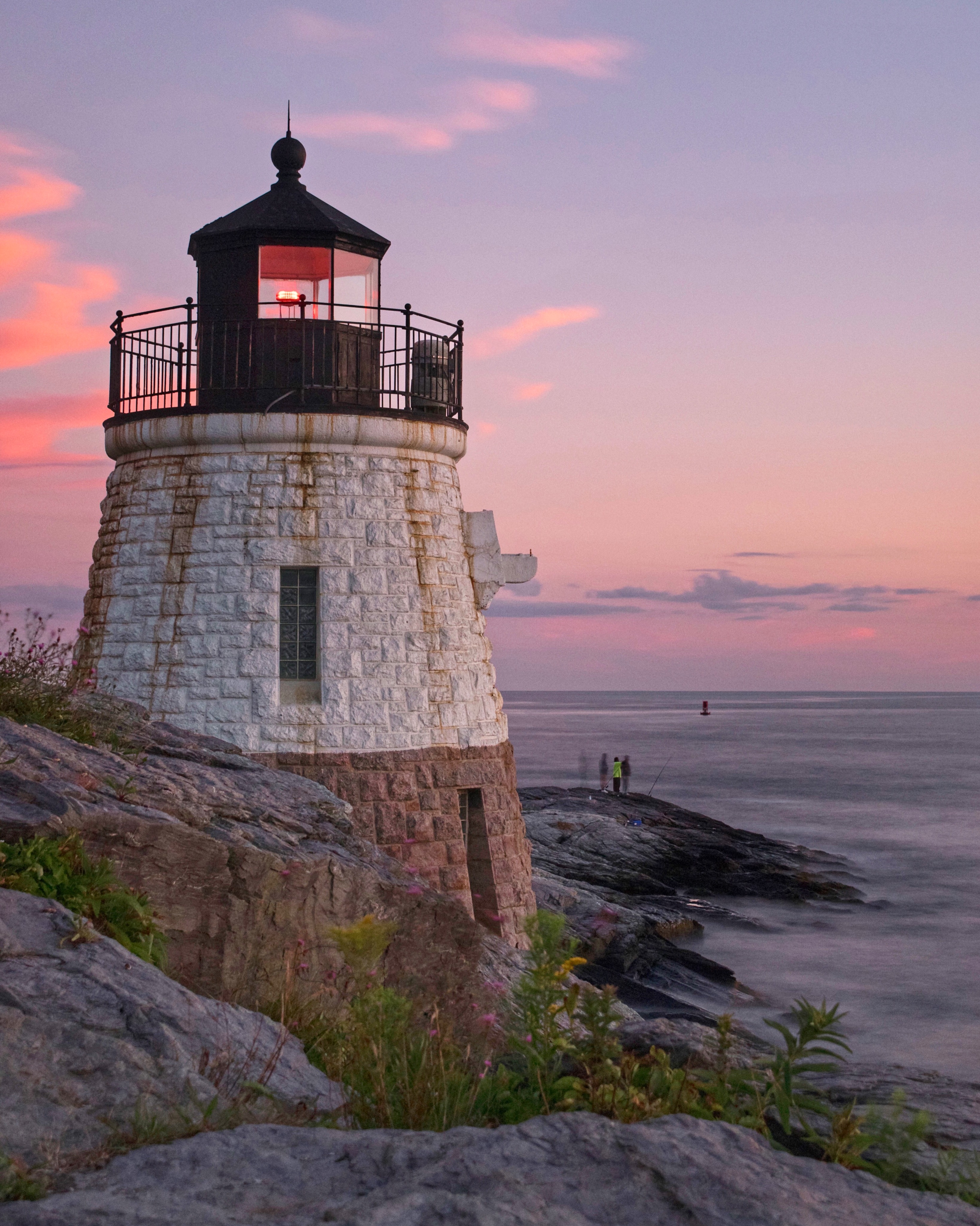 pastel skies behind a lighthouse on the water